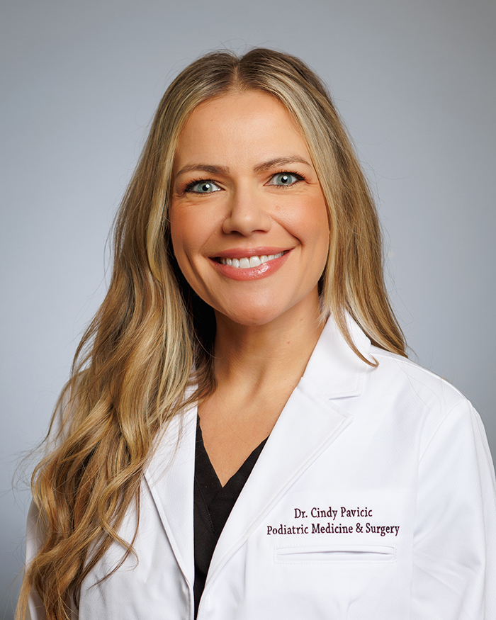 A smiling woman wearing a white lab coat with name and title, posing for a professional portrait.