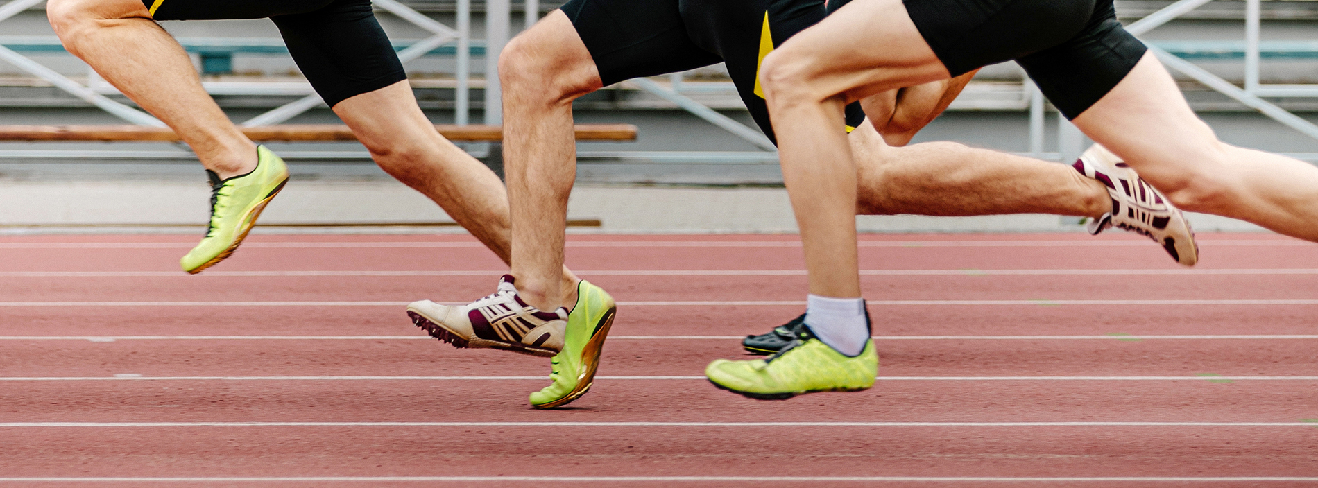 Two male athletes in sportswear, one wearing a black uniform and the other a yellow uniform, competing in a running race on an outdoor track.