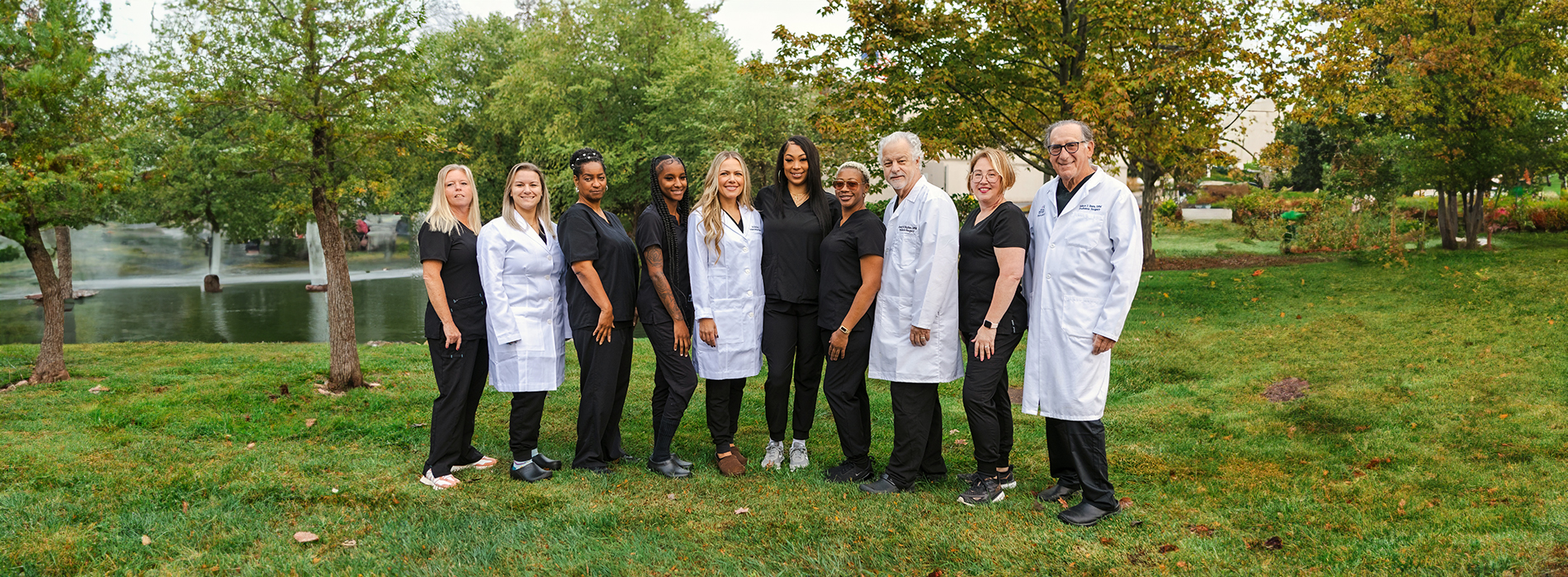 A group of six individuals, likely medical professionals, posing for a photograph in an outdoor setting with trees and grass visible.