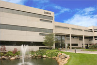 The image shows a modern multi-story building with a large glass facade, featuring a prominent sign that reads  SUNOCO,  situated in a landscaped area with a water feature and trees.