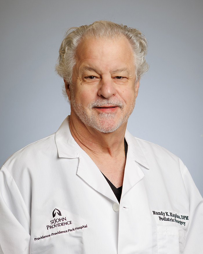 The image shows a man wearing a white lab coat, posing for a portrait with a professional background.