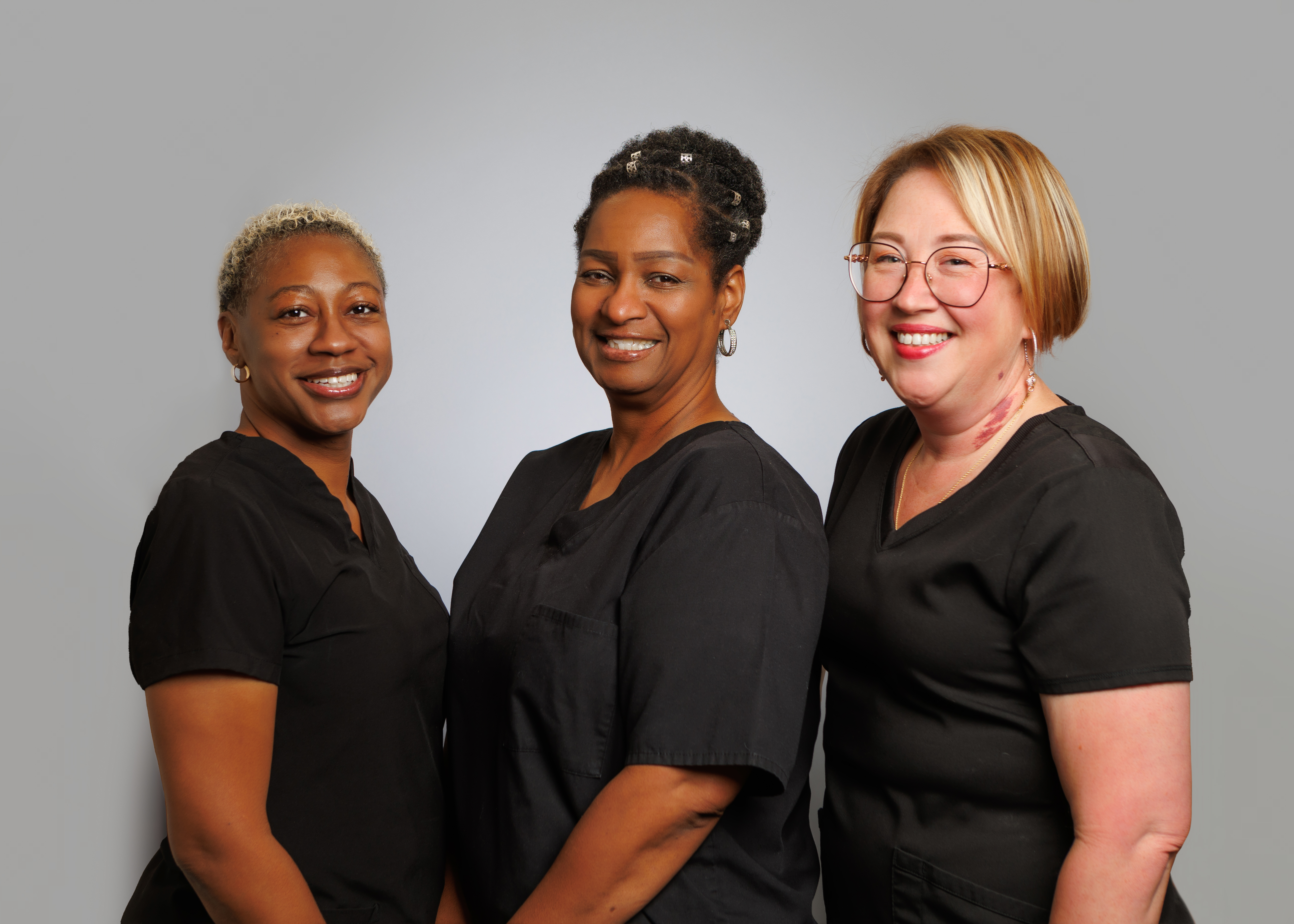 The image features three individuals, two women and a man, dressed in professional attire, standing side by side with smiles on their faces. They appear to be posing for a formal portrait, likely related to their work in the medical field.
