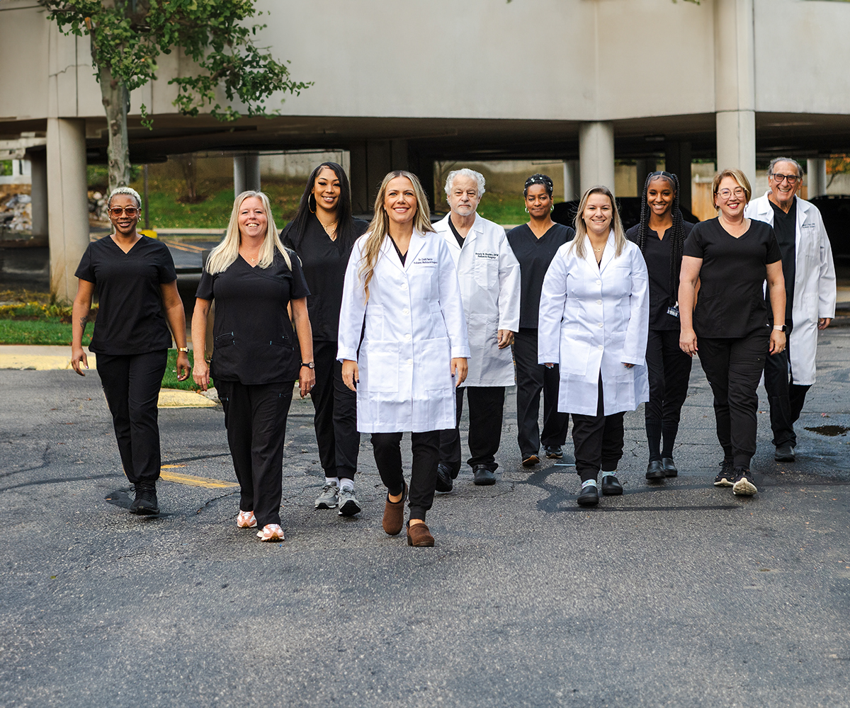 A group of healthcare professionals, including a man in a white lab coat, posing together in a parking lot.