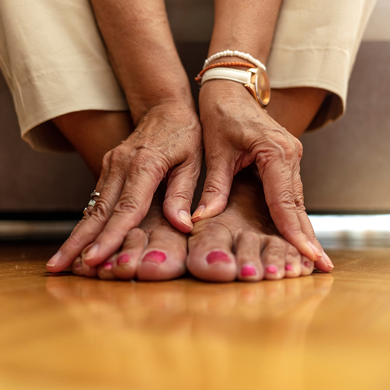 A person with their feet crossed and hands resting on the floor, wearing pink nail polish.